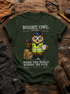 Green t-shirt with an owl graphic and text on a wooden surface with work-related items. Night Owl Division warehouse owl wearing a safety vest, holding a barcode scanner and coffee cup, with the slogan When the World Sleeps We Pick.